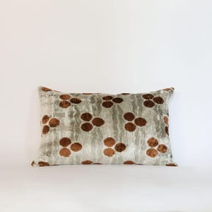 May include: Rectangular decorative pillow with a light gray background and a repeating pattern of brown floral-like shapes. The pillow has a soft, textured appearance, and the design is evenly spaced across the surface.