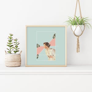 May include: A square framed art print featuring a collage of a person in a light-colored shirt positioned between two cameras. The background is a soft mint green with a pink triangular shape behind the person. Dotted white lines connect the cameras.