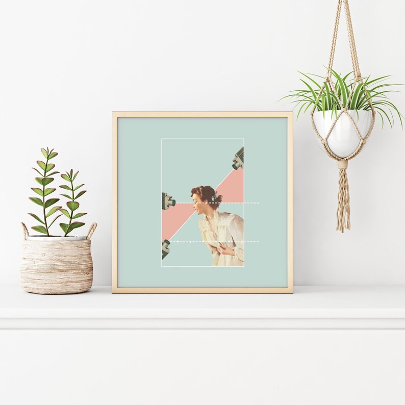May include: A square framed art print featuring a collage of a person in a light-colored shirt positioned between two cameras. The background is a soft mint green with a pink triangular shape behind the person. Dotted white lines connect the cameras.