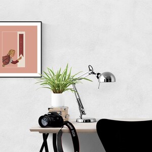 May include: A square framed wall art print featuring a muted pink background and a vertical rectangular panel. The illustration depicts a person with blonde hair wearing a red jacket, reaching toward a white arrow pointing upward with the word SWIPE.