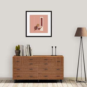 May include: A framed square art print featuring a person with blonde hair reaching toward a vertical red rectangle on a dusty pink background. The print is displayed above a wooden dresser with ten drawers, a potted cactus, books, and two black candlesticks.