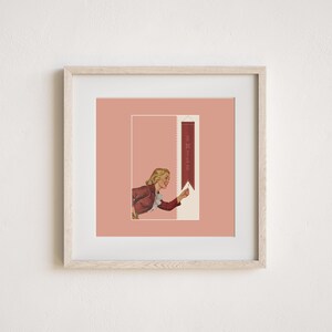 May include: A framed square print featuring a light pink background with a central illustration of a blonde person in a red jacket pointing toward a vertical dark red banner that contains the word SMILE in light-colored capital letters.