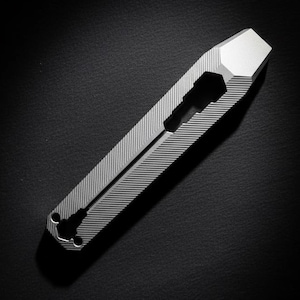 May include: A silver multi-tool with a hexagonal head and a ridged body. The tool has a slot and two circular openings at the base. The background is black.