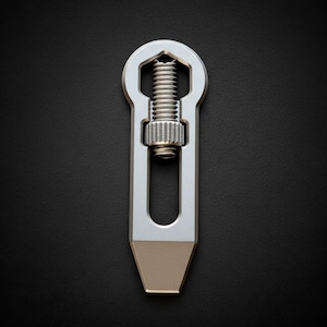 以下が含まれることがあります： ネジ機構とベージュ色の先端を備えたシルバーの金属製ツール。ツールは鍵穴型のトップとスロット付きの長方形のボディを備えています。背景は黒です。