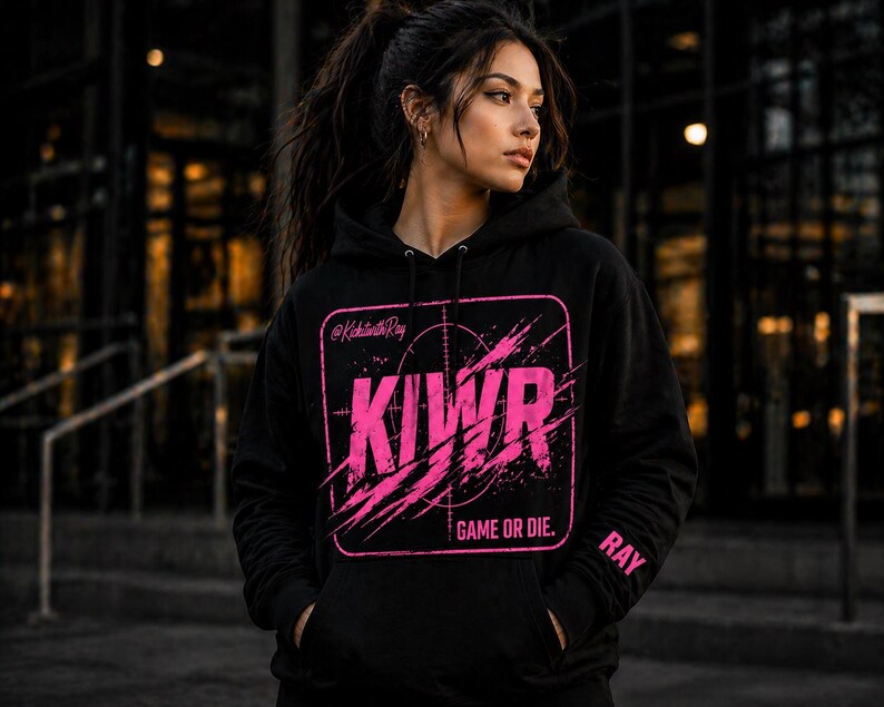 May include: Black hoodie with a pink graphic design. The design includes the letters "KIWR" inside a square with a target reticle and the words "GAME OR DIE." The sleeve has the name "RAY" printed on it. The hoodie has a drawstring hood and a front pocket.