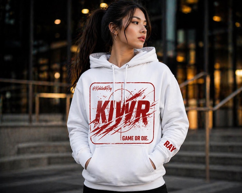 May include: White hoodie with a red graphic design. The design includes the letters "KIWR" inside a rectangular frame with a target and splatter effect. The text "GAME OR DIE." is below the graphic. The sleeve has the name "RAY".