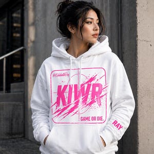 May include: White hoodie with a pink graphic design. The design includes the letters KIWR inside a square with a target reticle, and the words "GAME OR DIE." The sleeve has the name "RAY" printed on it.