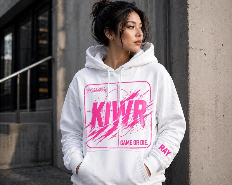 May include: White hoodie with a pink graphic design. The design includes the letters KIWR inside a square with a target reticle, and the words "GAME OR DIE." The sleeve has the name "RAY" printed on it.