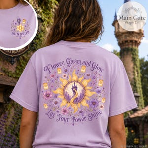 May include: A light purple t-shirt featuring a large graphic on the back with a yellow sun, a purple tower, floating lanterns, and purple flowers. The text reads, "Flower, Gleam and Glow, Let Your Power Shine." A smaller matching logo is on the front.
