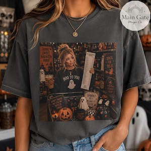 May include: A charcoal gray short-sleeve t-shirt featuring a graphic print of a person holding a long receipt in a store filled with Halloween decor. The print includes text such as Boo To You, Home Sweet Haunted Home, and Trick Or Treat.