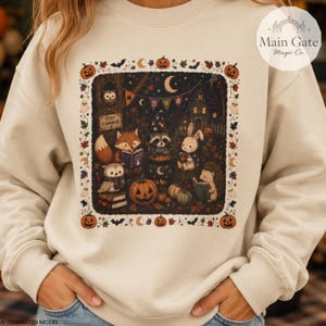 May include: A cream-colored sweatshirt featuring a central rectangular graphic of woodland animals in a forest setting at night. The illustration includes a fox, raccoon, rabbit, owl, and hedgehog with pumpkins, books, and a sign reading Stay Curious.