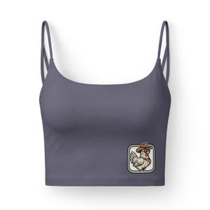 May include: A grey crop top with thin straps. A rectangular patch on the front features a cartoon chicken wearing a cowboy hat and a red bandana. The patch is outlined with a rope-like border.
