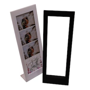 May include: A white photo frame with three vertical photo slots, displaying a wedding photo strip. The frame has a decorative floral design and the name "Smith" in cursive. A separate black frame stands beside it.