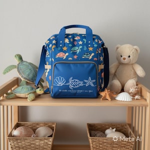 May include: A blue backpack featuring a repeating pattern of sea turtles, starfish, and seashells. The front pocket displays a white line-art graphic of a seashell, a turtle, and a starfish with the text Be still and know that I am God.