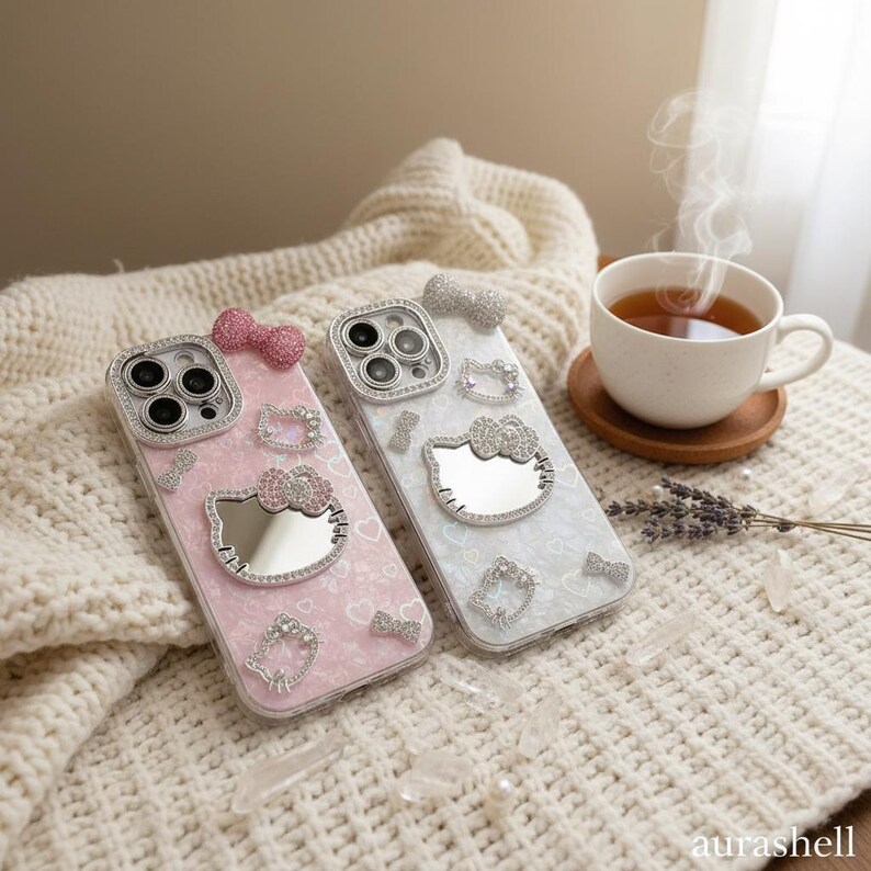 Może przedstawiać: Dwa dekoracyjne etui na telefon z motywami Hello Kitty. Jedno etui jest r&oacute;żowe ze wzorem kokardki i serca, drugie białe. Oba etui mają lustrzaną twarz Hello Kitty i są ozdobione kryształkami.