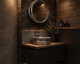 May include: A bathroom vanity featuring a round silver metal basin with blue star accents, a wooden countertop, and a dark slatted cabinet. Above the basin is a round silver mirror mounted on a dark brick wall with integrated lighting.