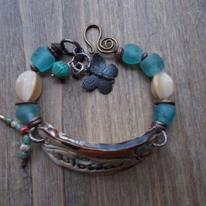 May include: A bracelet with a ceramic charm, turquoise and white beads, and a metal butterfly charm.