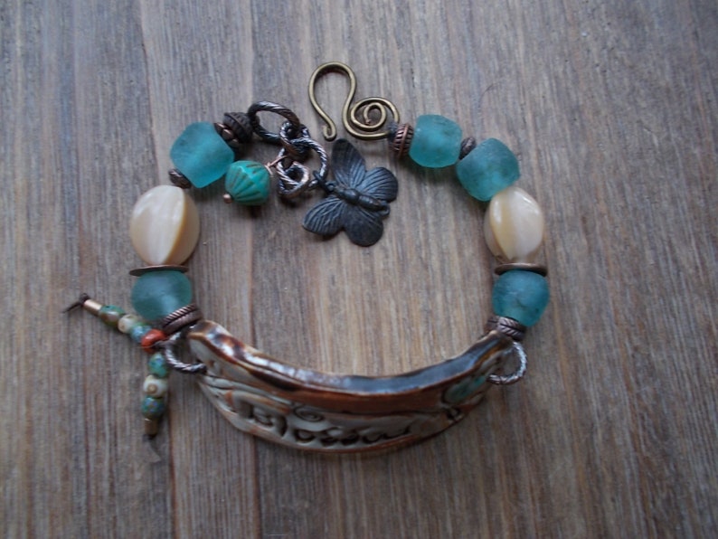 May include: A bracelet with a ceramic charm, turquoise and white beads, and a metal butterfly charm.