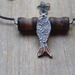 May include: A handcrafted ceramic fish pendant with blue and white swirl patterns, attached to a wooden corkscrew handle. The corkscrew is set against a wooden background, with a metal wire and decorative element.