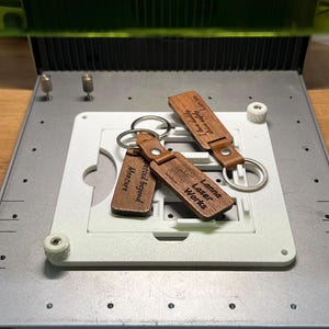 May include: Three wooden keychains with leather straps and silver key rings. Each keychain has engraved text. One reads "Blessed beyond Measure", another "I have safely driven Lisa too", and the third "Lanna Laser Works".