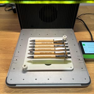 Può includere: Una macchina per incisione laser con un vassoio che contiene sei penne. Le penne sono in legno chiaro e hanno dettagli argentati. Ogni penna è incisa con il testo "Lanna Laser.shop" e "Laser Engraving & 3d Printing".