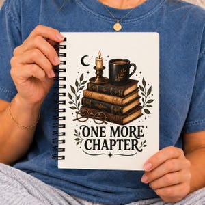 May include: A white spiral-bound notebook featuring a graphic of a stack of four books, a lit candle in a holder, a black mug, and round glasses. The text "ONE MORE CHAPTER" is printed in black below the illustration with decorative leaves.