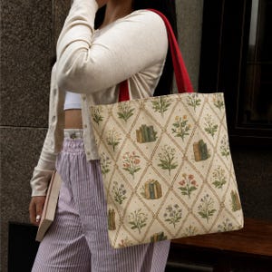 May include: A tote bag featuring a cream-colored fabric with a repeating diamond lattice pattern. Inside each diamond are illustrations of various colorful wildflowers and small stacks of books. The bag has two bright red shoulder straps.
