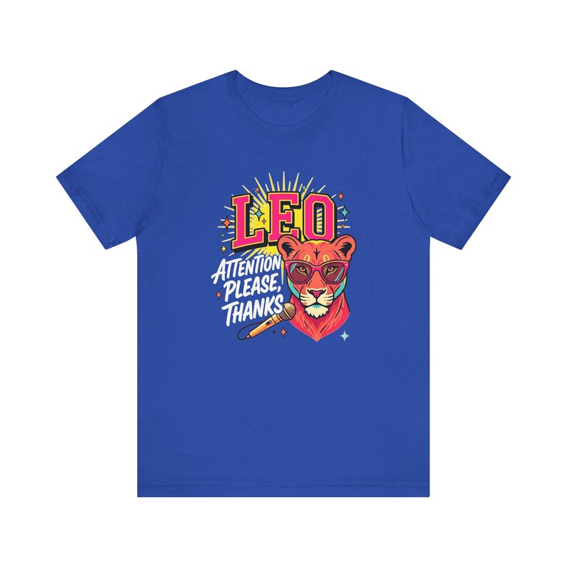 May include: A royal blue short-sleeve t-shirt featuring a graphic of a lion wearing pink glasses. The design includes the text LEO and ATTENTION PLEASE, THANKS, along with a microphone illustration and yellow sunburst rays behind the lion head.