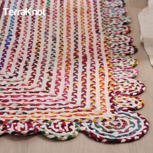 Op de afbeelding: Een kleurrijk gevlochten tapijt met een geschulpte rand. Het tapijt heeft verticale strepen in wit, rood, geel en blauw. De tekst "Terraknot" staat in de linkerbovenhoek. Het tapijt is gemaakt van geweven materiaal.