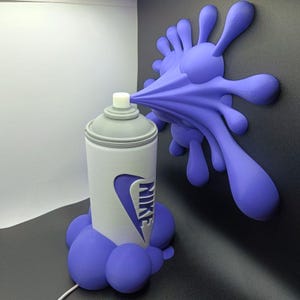 Può includere: Scultura stampata in 3D di una bomboletta spray bianca e grigia con il logo Nike, che spruzza uno schizzo di vernice viola. Lo schizzo di vernice è attaccato a una parete nera e la bomboletta poggia su un gruppo di gocce di vernice viola.