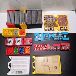 Può includere: Una collezione di organizzatori colorati per giochi da tavolo. Il set include contenitori rossi, gialli, blu e neri per carte, gettoni e componenti di gioco. Gli organizzatori sono progettati per contenere vari componenti del gioco.