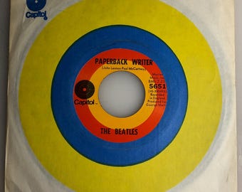 May include: A yellow and blue vinyl record with the text "PAPERBACK WRITER (John Lennon-Paul McCartney)" and "THE BEATLES" on it. The record is labeled "Capitol" and has the song title, songwriters, and song information.