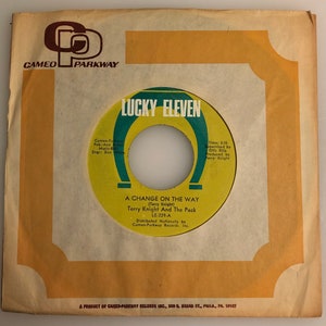 May include: A yellow and orange vinyl record with the title "Lucky Eleven" and the song title "A Change On The Way" by Terry Knight And The Pack. The record label is Cameo-Parkway Records.