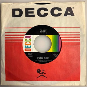 May include: Vintage 45 RPM record by Patsy Cline in a red and white DECCA sleeve. The record label is black with the song title "Crazy" and a colorful stripe design. The sleeve has the DECCA logo.