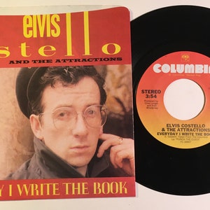 May include: A black vinyl record with a red and white label. The label says "Columbia" and features the song "Everyday I Write The Book" by Elvis Costello and The Attractions. The record is 3:54 long.