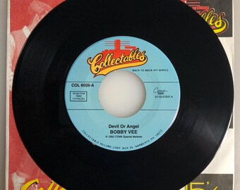 May include: A black vinyl record with a blue and white label. The label says "Collectables" and "Back to Back Hit Series". The record is titled "Devil Or Angel" by "Bobby Vee".