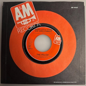 May include: A vintage 45 RPM vinyl record by The Police, titled "Every Little Thing She Does Is Magic." The record is in its original orange and black sleeve, featuring the A&M Records logo. The record label is orange with black text.