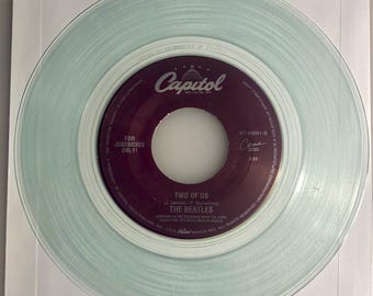 May include: A light blue vinyl record with a purple label. The label has the text "Capitol" in white, "Two of Us" in white, "The Beatles" in white, and "For Jukeboxes Only!" in white. The record number is "57-10891-8".