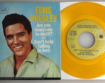May include: A yellow vinyl record with the text "Elvis Greatest Hits Golden Singles Vol. 2" and "Can't Help Falling in Love Elvis Presley with The Jordanaires". The record is on a white background with a picture of Elvis Presley on the left side of the image.