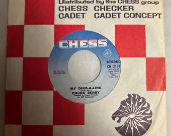 May include: A vintage vinyl record for "My Ding-A-Ling" by Chuck Berry, featuring a blue and silver label with the "CHESS" logo. The record is in its original sleeve, which has a red and white checkered pattern.