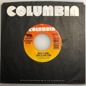 Può includere: Un disco in vinile rosso e bianco con il titolo "Billy Joel This Is The Time" e la durata della canzone "4:56". Il disco è della casa discografica Columbia ed è stato prodotto da Phil Ramone.