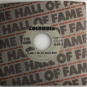 May include: A black and white 45 RPM vinyl record by Eydie Gorme. The record is titled "Blame It On The Bossa Nova" and features the Columbia Records label. The record was released in December 1962.