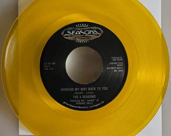 May include: A translucent yellow vinyl record featuring the song "Working My Way Back To You" by The 4 Seasons. The record label is black with white text, including the band's name and song title. The record is from Four Seasons Record Co. Los Angeles CA.