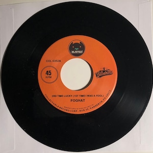 May include: A black vinyl record with an orange label. The label has the text "COL 0352A", "45 RPM", "3RD TIME LUCKY (1ST TIME I WAS A FOOL)", "FOGHAT", "COLLECTABLE RECORD CORP., BOX 35, NARBERTH, PA 19072", and "MANUFACTURED BY RHINO RECORDS INC".