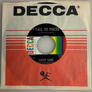 May include: A vintage 45 RPM vinyl record by Patsy Cline, titled "I Fall to Pieces." The record is in a paper sleeve with the Decca Records logo and red and white stripes. The record label features a colourful design.