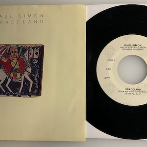 May include: A 7-inch vinyl record by Paul Simon, featuring the song "Graceland" from his album of the same name. The record is black with a white label that includes the song title, artist name, and production information.