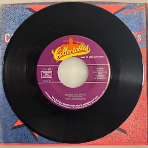 May include: A black vinyl record featuring the song "I Want You Back" by The Jackson 5. The record label is purple and gold with the Collectables logo. The record is in its original sleeve, which has a red and blue design.