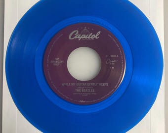 May include: A blue vinyl record for jukeboxes, featuring the song "While My Guitar Gently Weeps" by The Beatles. The record label is purple with white text and the Capitol Records logo.
