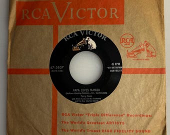 May include: Vintage 45 RPM vinyl record for "Papa Loves Mambo" by Perry Como, featuring the RCA Victor logo. The record is in its original brown paper sleeve with orange text and graphics, including "New Orthophonic High Fidelity."