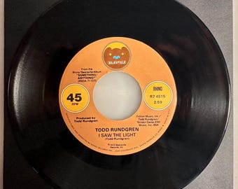 May include: A black vinyl record with an orange and white label. The label features the text "TODD RUNDGREN I SAW THE LIGHT" and the Rhino Records logo. The record is a 45 RPM single.